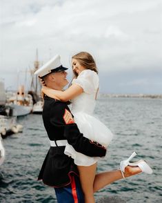 a man in uniform is holding a woman on his back by the water's edge