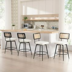 four stools in front of a kitchen island with white counter tops and wooden flooring