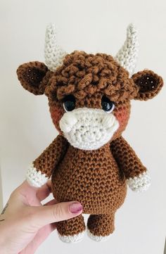 a crocheted brown and white cow with big horns is held up to the camera