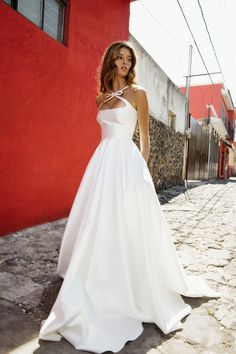 a woman in a white wedding dress standing on the side of a road next to a red building