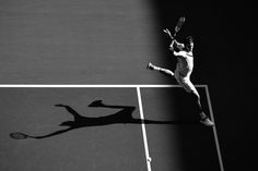 black and white photo of a man playing tennis on a court with shadow from his racket