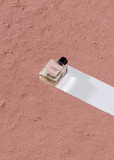 a bottle of perfume sitting on top of a piece of paper next to a pink wall