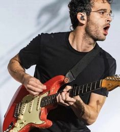 a man playing an electric guitar while wearing glasses and a black t - shirt with his mouth open