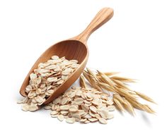 a wooden spoon full of oats next to some ears of oats on a white background