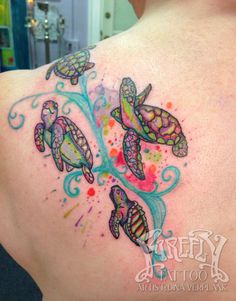 the back of a woman's shoulder with three turtles on it and watercolor paint splatters