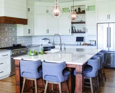 a large kitchen with white cabinets and an island in the middle, surrounded by blue chairs