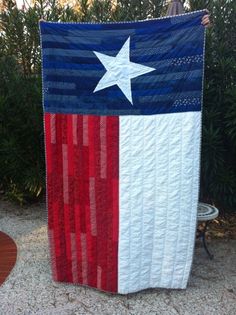 an american flag quilt is displayed in front of some bushes