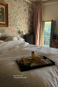 a tray with food on top of a bed next to a window in a bedroom