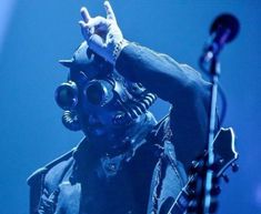 a man wearing a gas mask and holding his hand up in the air while standing next to a microphone