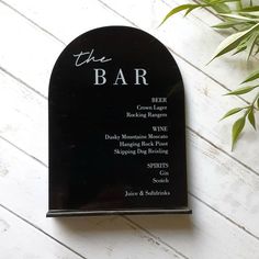 the bar business card on top of a white wooden table next to a potted plant