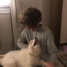 a person sitting on the floor petting a white cat with its mouth wide open