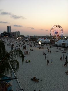 many people are on the beach at sunset with ferris wheel in the distance and buildings behind them