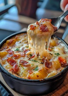 a person holding a fork full of cheese and tomato casserole in a skillet