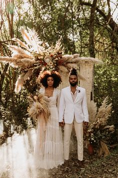 a man and woman standing next to each other in front of some trees with feathers on them