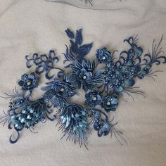 an embroidered piece of cloth with blue flowers and leaves on the side, sitting on a bed