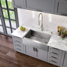 a stainless steel kitchen sink with marble countertops and gray cabinets in a home setting