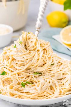 a fork full of spaghetti being lifted from a white bowl with lemons in the background