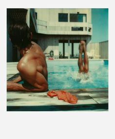 two people are swimming in a pool with towels on the ground and one person has his back turned to the camera