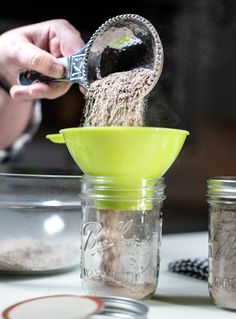 a person pouring sand into a mason jar with a green strainer on the side