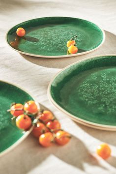 three green plates with oranges on them sitting on a white tablecloth covered table