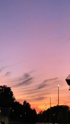 the sky is purple and pink at dusk with cars parked on the street in front