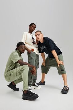 three young men are posing for the camera in green pants and black shoes, one is leaning on his knee