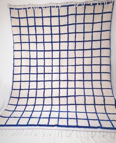 a blue and white pillow with fringes on it's edges, sitting against a wall