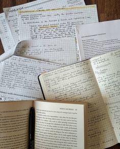 an open book sitting on top of a wooden table next to some papers and a pen