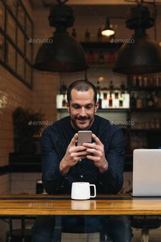 a man sitting at a table looking at his cell phone while holding a coffee mug