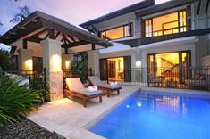 a house with a swimming pool and lounge chairs in front of it at night time