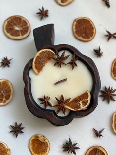 an orange slice and star anise candle surrounded by cinnamons on a white surface