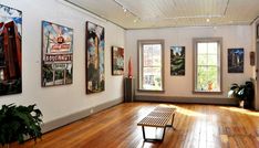 an empty room with wooden floors and paintings on the wall, along with a bench