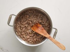 a wooden spoon sitting in a pot filled with ground beef and seasoning next to a white counter top