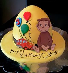 a yellow birthday cake with a monkey on top and balloons in the shape of a firetruck