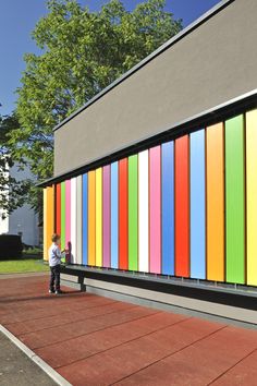 a little boy standing in front of a building with multicolored stripes on it