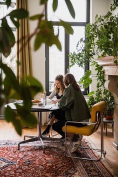 two women sitting at a table in front of a window