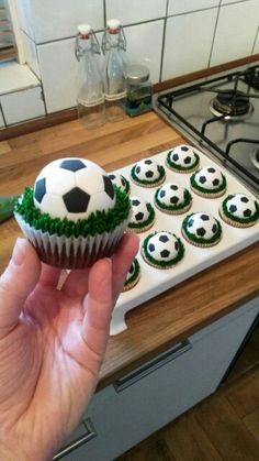 a person holding a cupcake with soccer balls on it in front of a stove