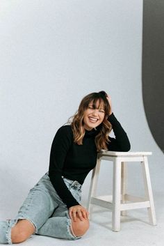 a smiling woman sitting on the ground next to a stool and posing for a photo