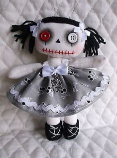 a stuffed doll with black hair and red eyes wearing a dress on top of a white quilt