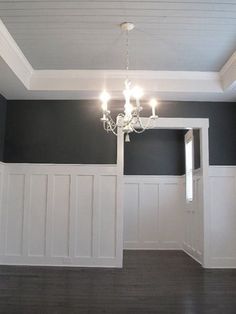 an empty room with white paneling and chandelier