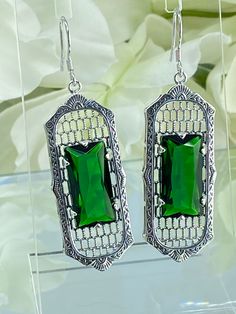 a pair of earrings with green stone in the center and silver filigrees