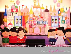 a group of children are standing in front of a birthday cake with balloons and decorations