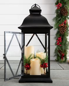 two lit candles sitting on top of a table next to christmas wreaths and pine cones