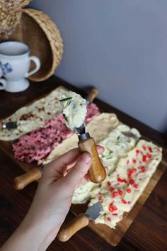 a person is holding a knife in front of a cake on a cutting board with other items