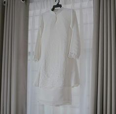 a white dress hanging on a window sill in front of drapes and curtains