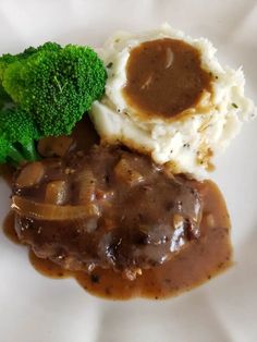 a white plate topped with mashed potatoes and gravy next to broccoli