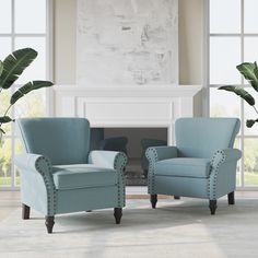 two light blue chairs in front of a fireplace with large windows and potted plants