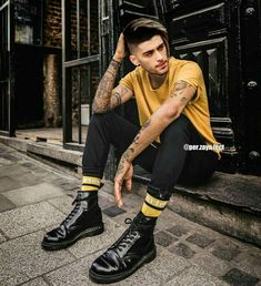 a young man sitting on the ground wearing black shoes and yellow socks with his hands in his pockets