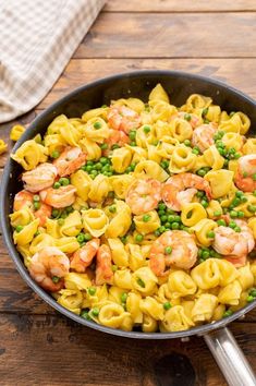 a skillet filled with shrimp tortellini and peas on top of a wooden table