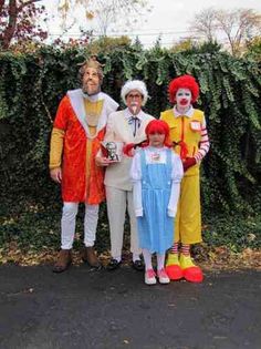 three adults and two children dressed up as clowns in front of a hedge wall